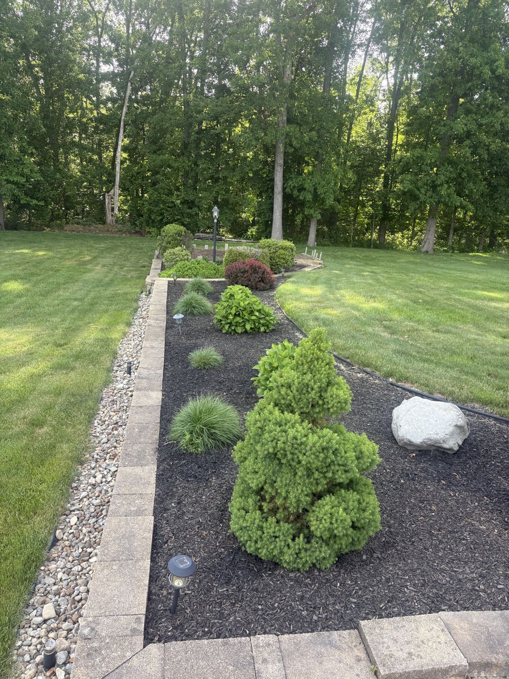 Freshly mulched garden bed with trimmed shrubs, stone border and striped lawn