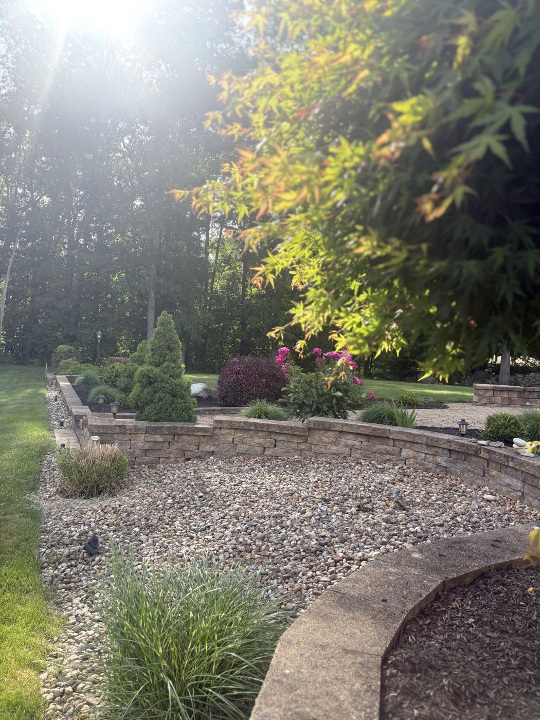 River stone bed below a curved retaining wall with ornamental grasses